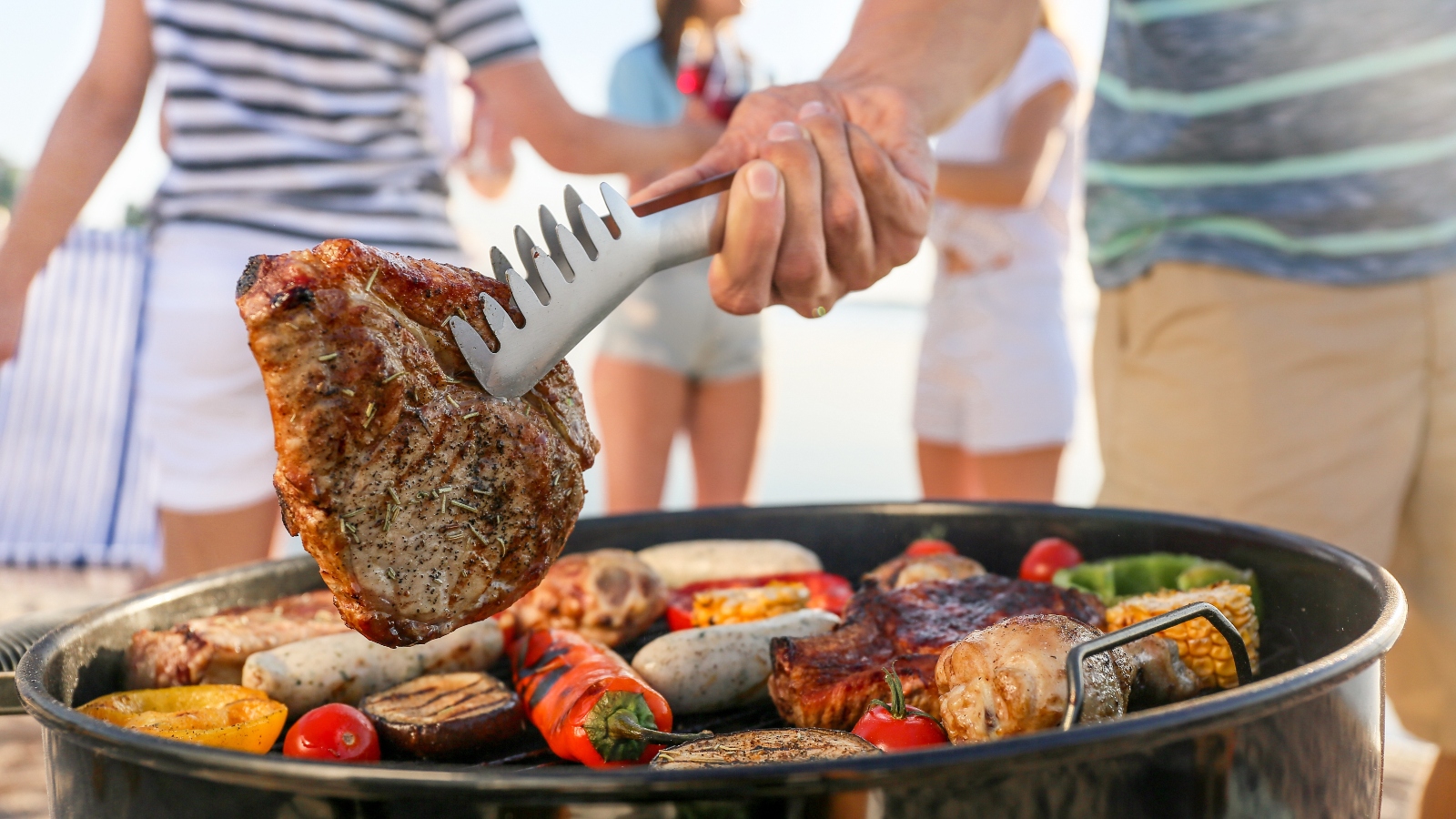 A person holds steak with metal tongs over a barbecue