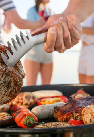 A person holds steak with metal tongs over a barbecue