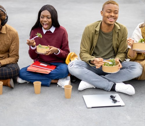 Students sit on the ground eating salad with their text books