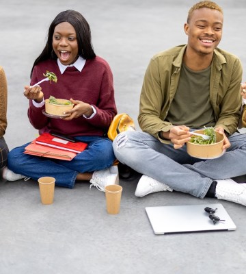 Students sit on the ground eating salad with their text books