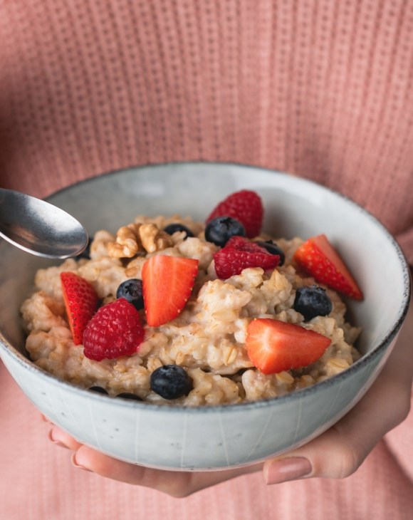 A person wearing a pink jumper holds a bowl of fruit and oatmeal