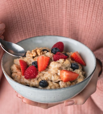 A person wearing a pink jumper holds a bowl of fruit and oatmeal