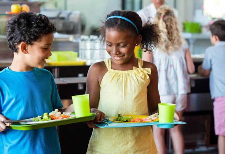 Children at school carrying trays of healthy food and smiling