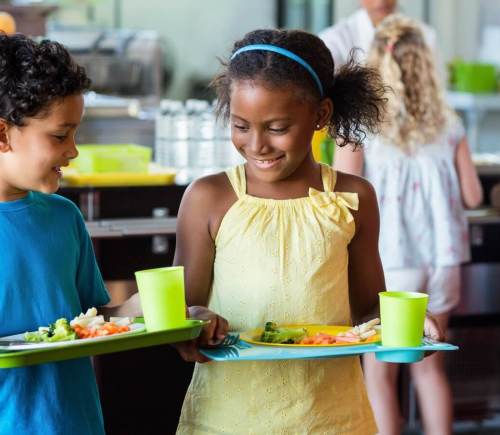 Children at school carrying trays of healthy food and smiling