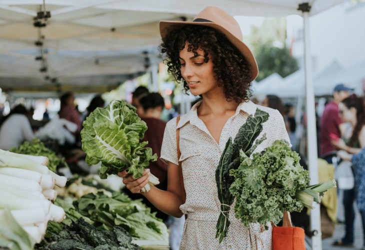 A person choosing between two vegetables at a market