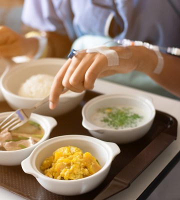 Woman wearing a blue dress, eating on the bed in the hospital